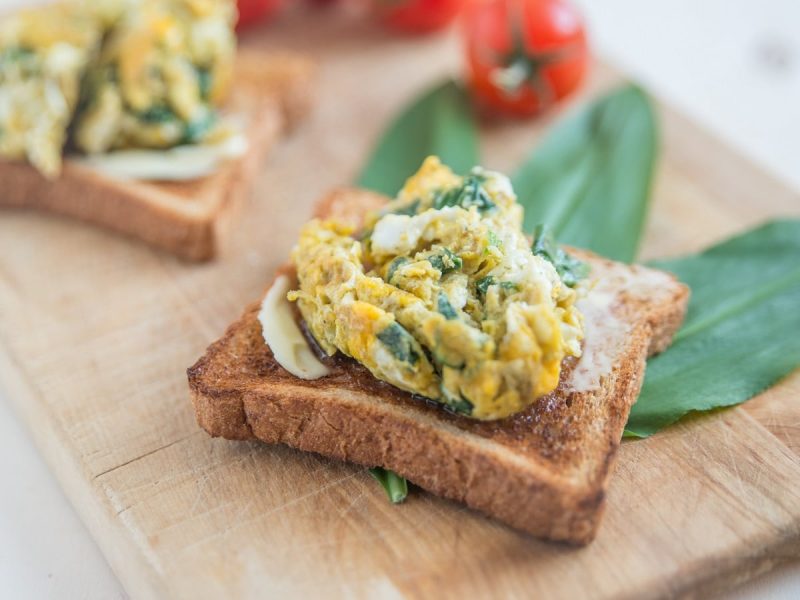 Zwei Toastbrote mit Bärlauch-Rührei auf einem Holzbrett.