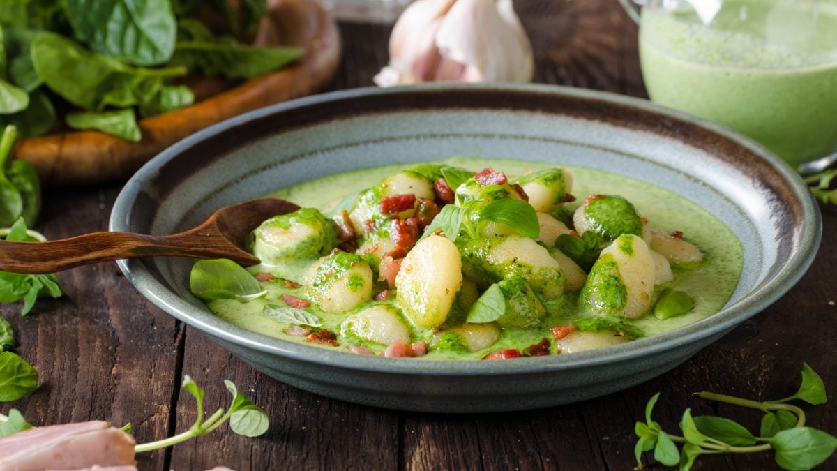 Eine blau-grauer Teller mit der Bärlauchsuppe und weißen Riesenbohnen auf einem dunklen Holztisch.