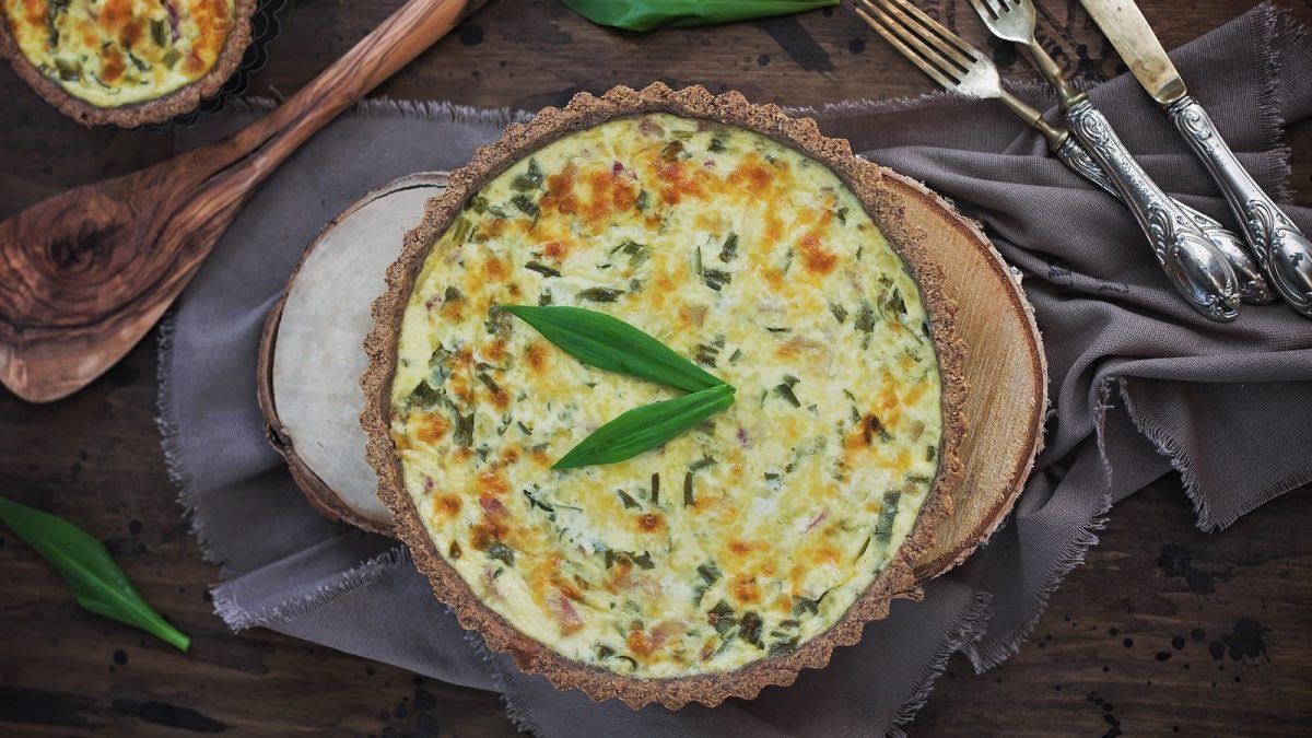 Eine Tarteform mit Bärlauch-Quiche neben Besteck.