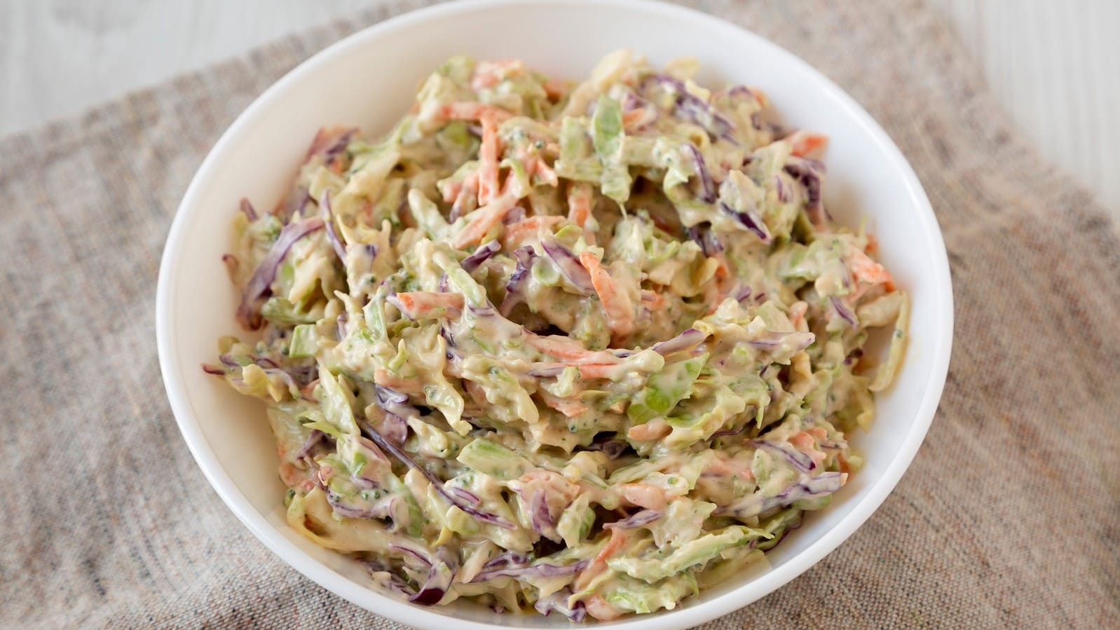 Ein weißer Teller mit Brokkoli Slaw auf einem beigen Küchentuch.