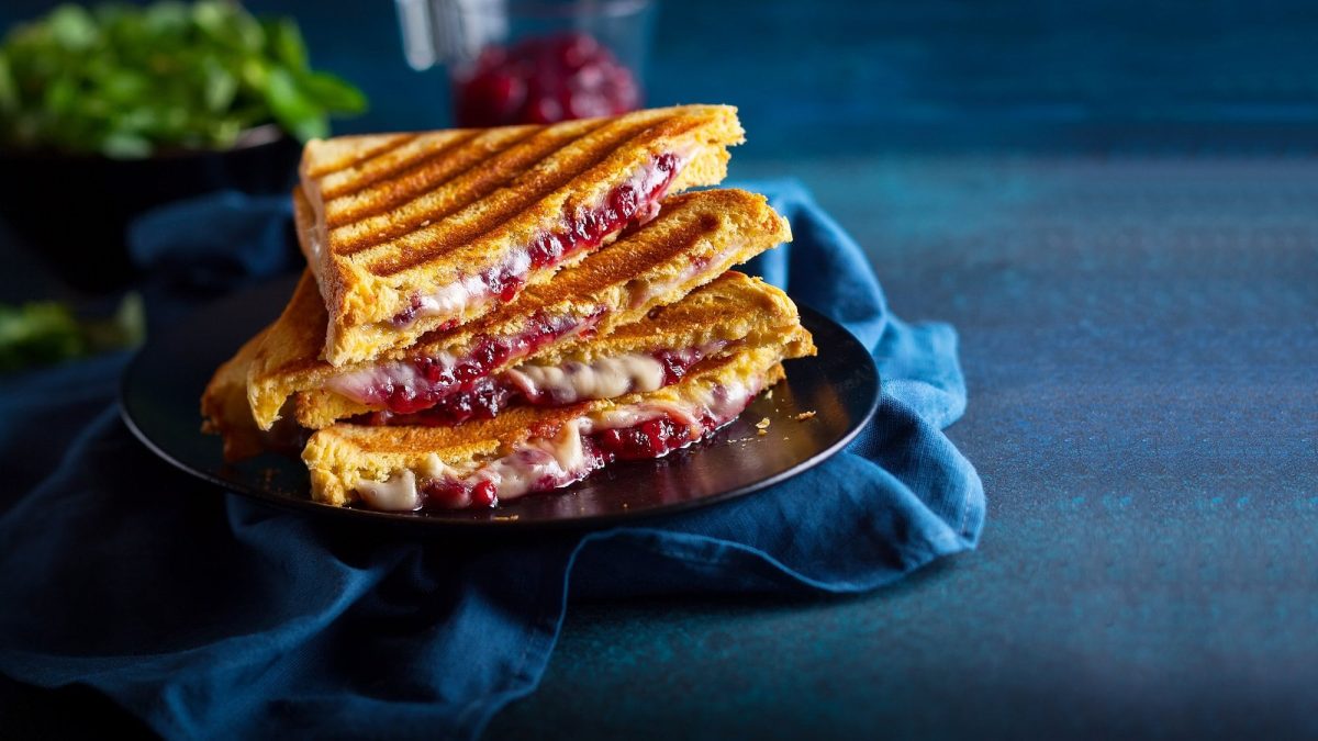 Frontal: zwei schräg angeschnittene Cheddar-Toasts mit Zwiebel-Chutney auf blauem Untergrund.