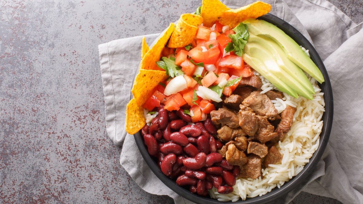 Chifrijo mit Chicharrón, Avocado, Tortilla-Chips, Bohnen und Reis in einer Schüssel auf grauem Tuch und Untergrund. Draufsicht.