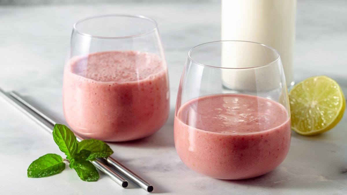 Zwei Gläser mit Himbeer-Tahini-Shake neben frischen Limetten.