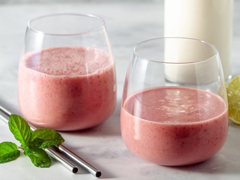 Zwei Gläser mit Himbeer-Tahini-Shake neben frischen Limetten.