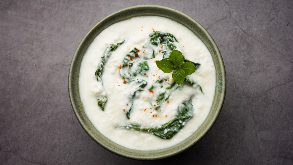 Eine hellgrüne Schüssel mit Palak Raita auf einem grauen Tisch.