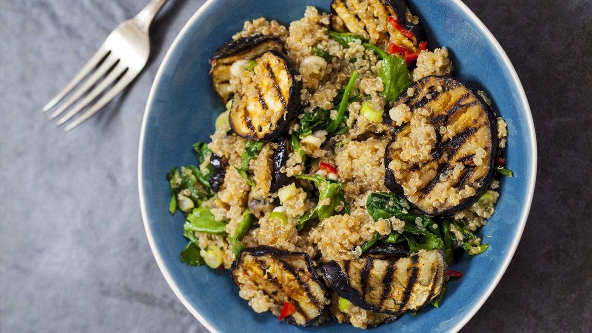 Eine blaue Schüssel mit Quinoa-Salat mit gegrillter Aubergine auf einem grauen Tisch.