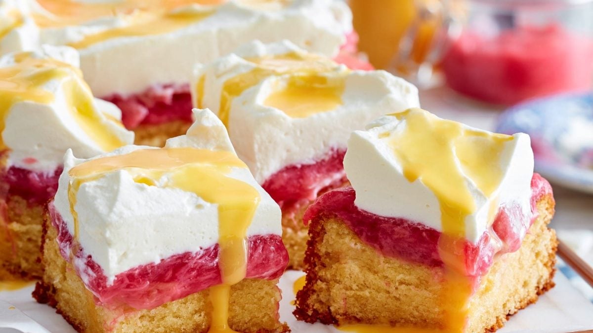 Mehrere quadratische Stücke Eierlikör-Rhabarbertorte mit Sahne, Hintergrund verschwommen.