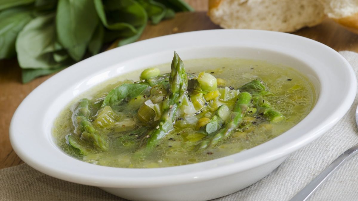 Ein weißer Teller mit Erbsensuppe und grünem Spargel.