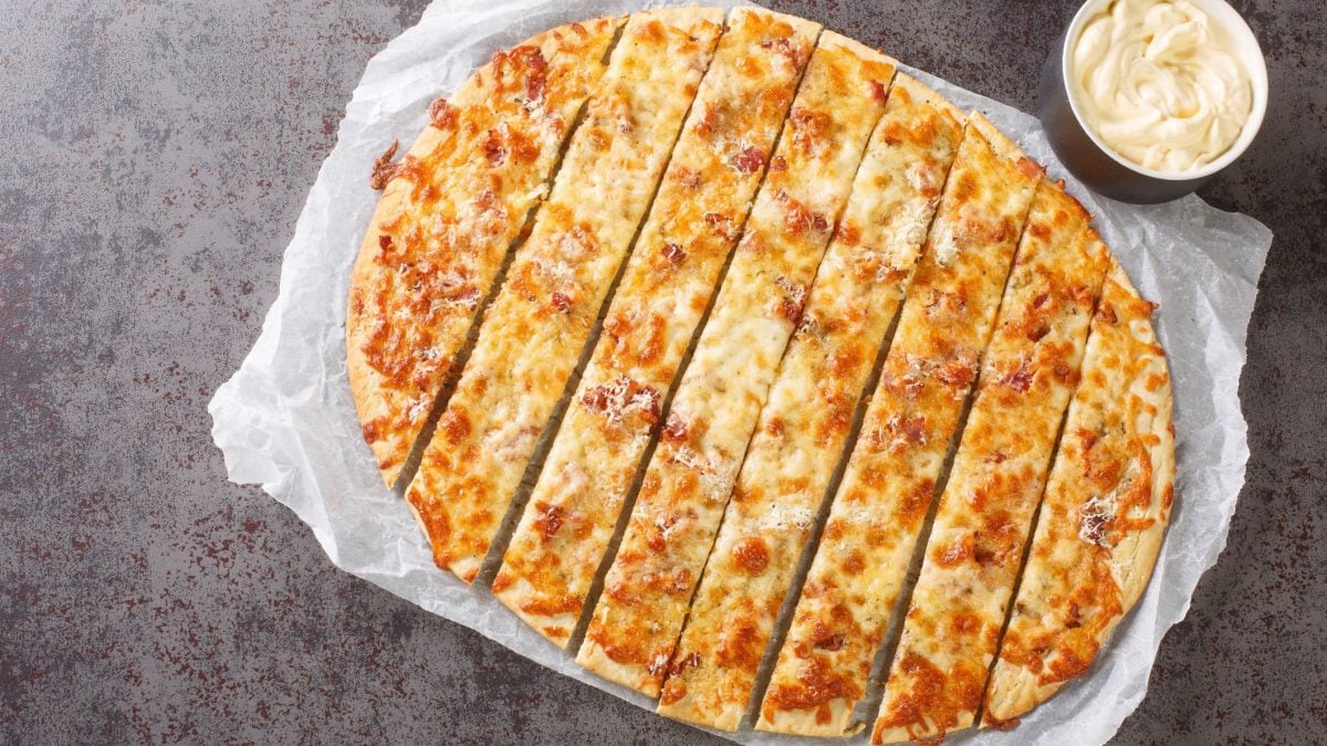 Garlic Fingers auf Backpapier auf grauem Untergrund. Daneben ein Dip.