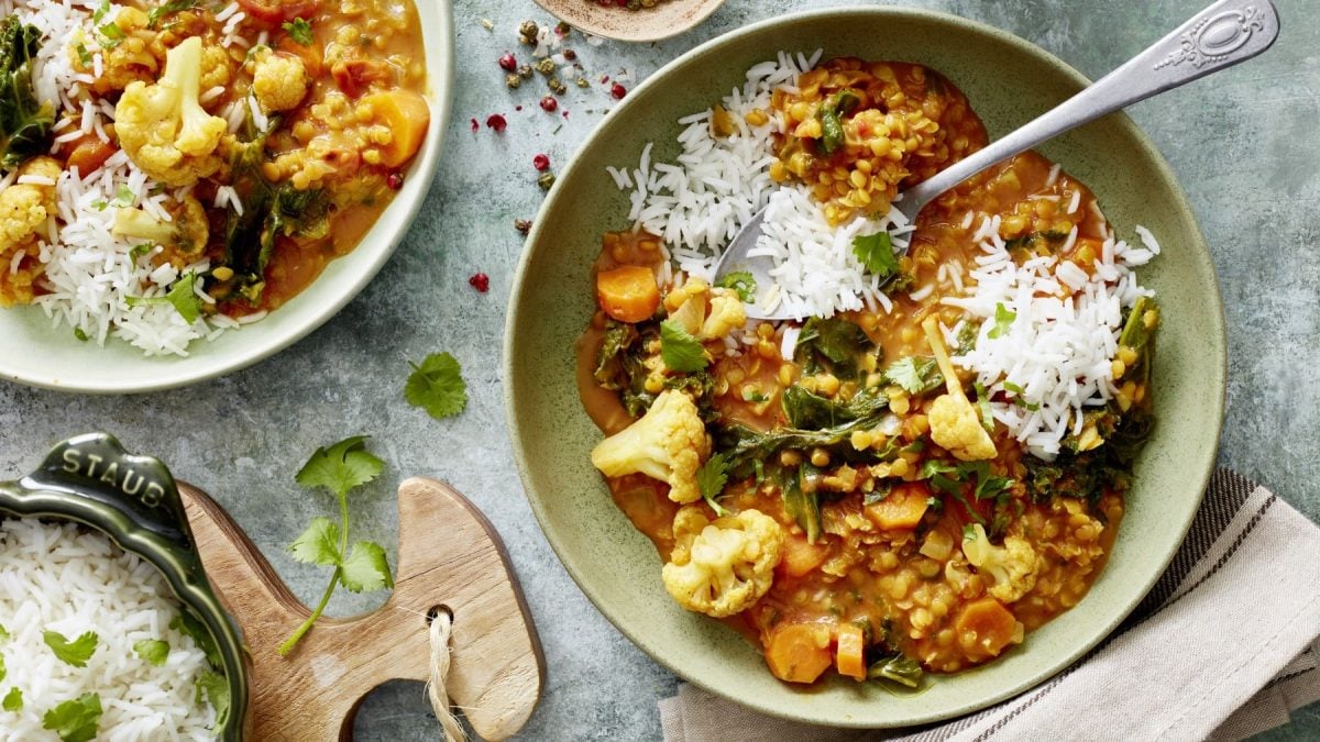 In einer Schüssel ist ein Grünkohl-Linsen-Curry angerichtet. Es wird mit Grünkohl, Tomaten und Ingwer verfeinert.