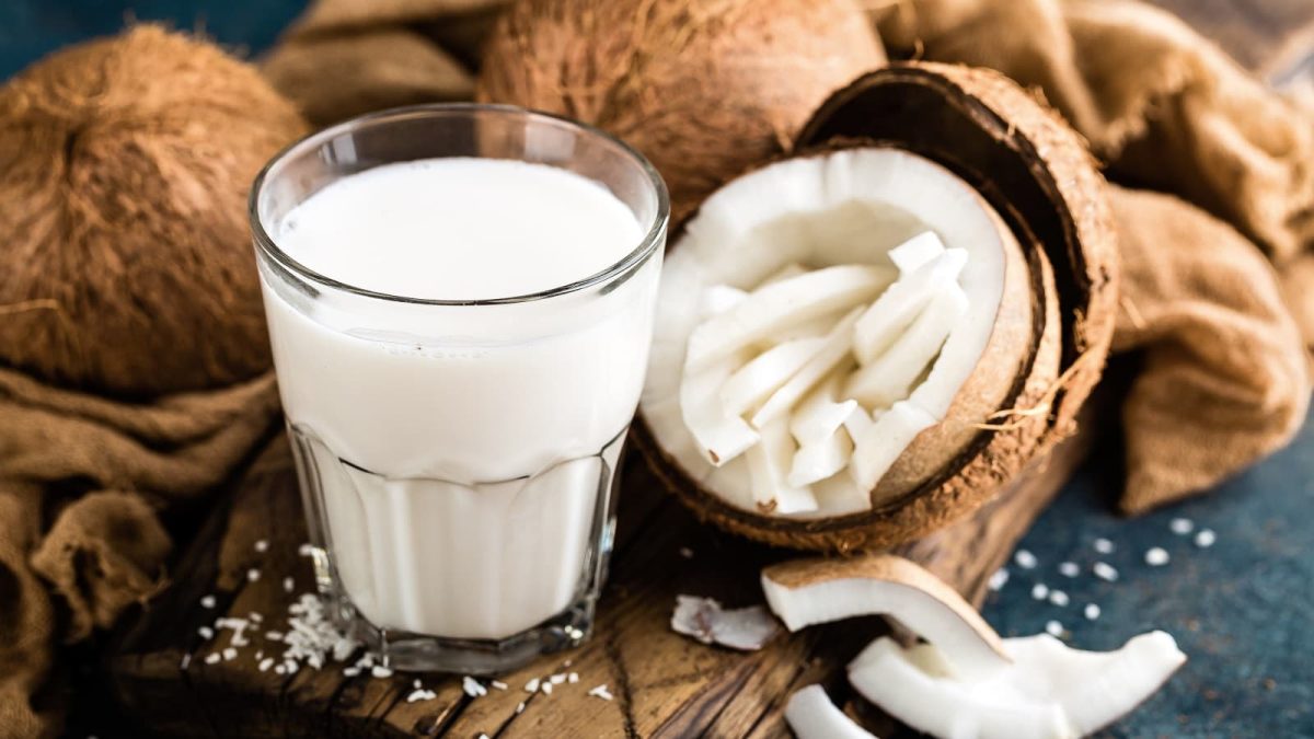 Ein Glas mit heißer Kokosschokolade neben einer frischen Kokosnuss.