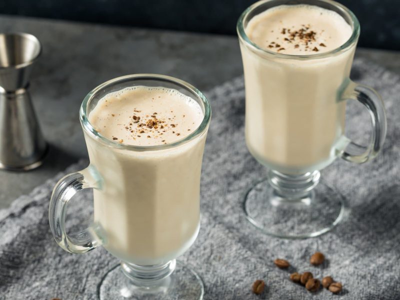Zwei Irish Coffee Milkshakes im Glas mit Barmaß und Kaffeebohnen auf grauem Untergrund. Draufsicht.