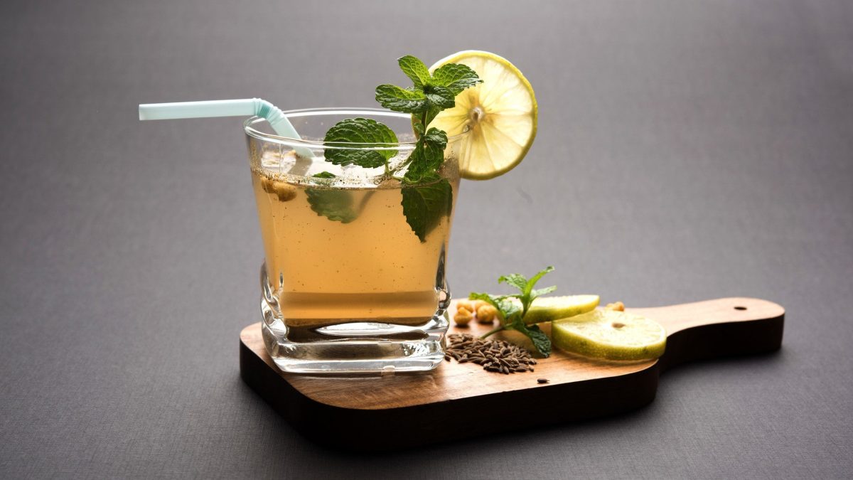 Jal Jeera oder Jaljeera mit Masala Kaltgetränk aus Indien mit Strohjalm, Limettenscheiben Minze und Boondi in Glas auf Holzbrett mit Deko. Frontalansicht.