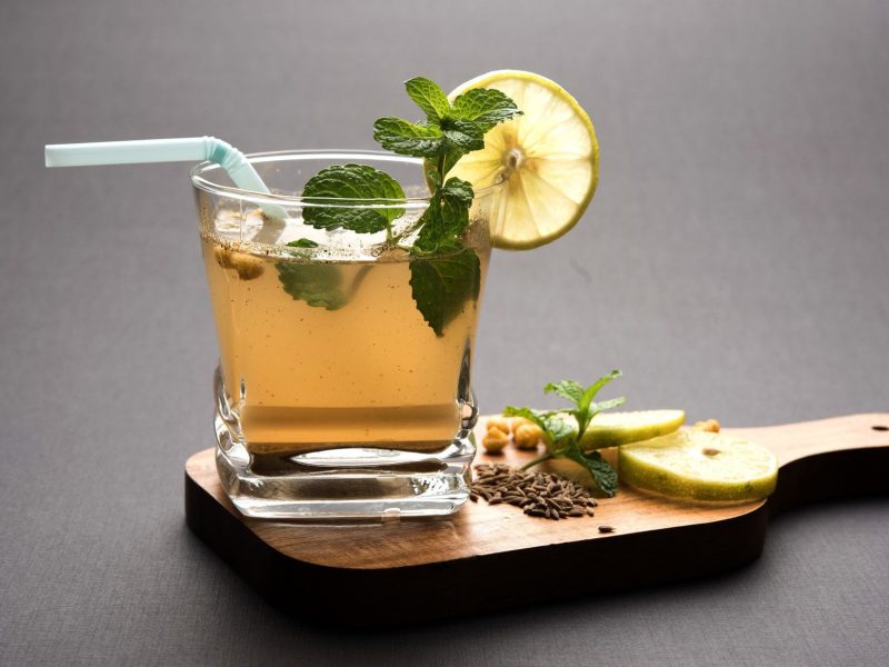 Jal Jeera oder Jaljeera mit Masala Kaltgetränk aus Indien mit Strohjalm, Limettenscheiben Minze und Boondi in Glas auf Holzbrett mit Deko. Frontalansicht.