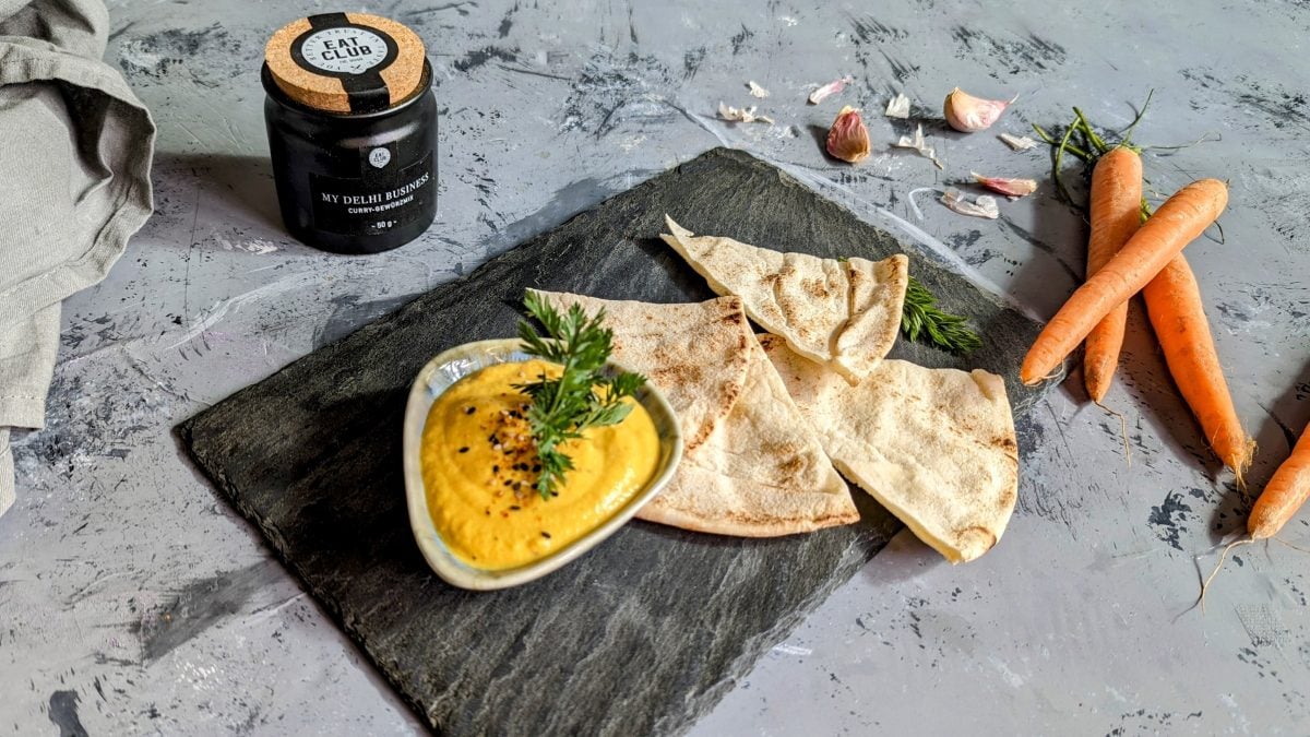Eine schwarze Schieferplatte auf grauem Untergrund mit der Karotten-Currycreme und Fladenbrot.