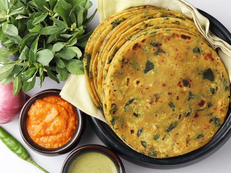 Ein schwarzer Teller mit Methi Paratha neben frischen Zutaten.
