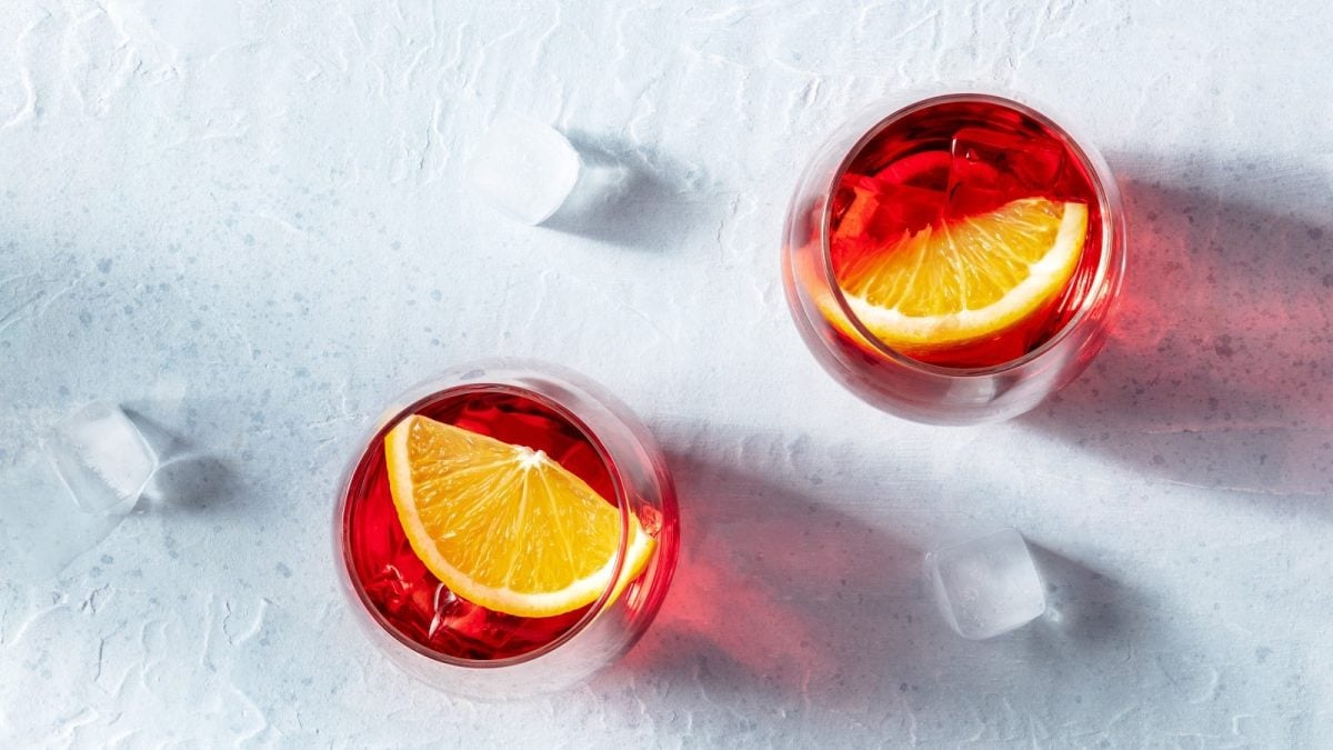 Zwei Gläser Negroni Spritz auf einem weißen Tisch.