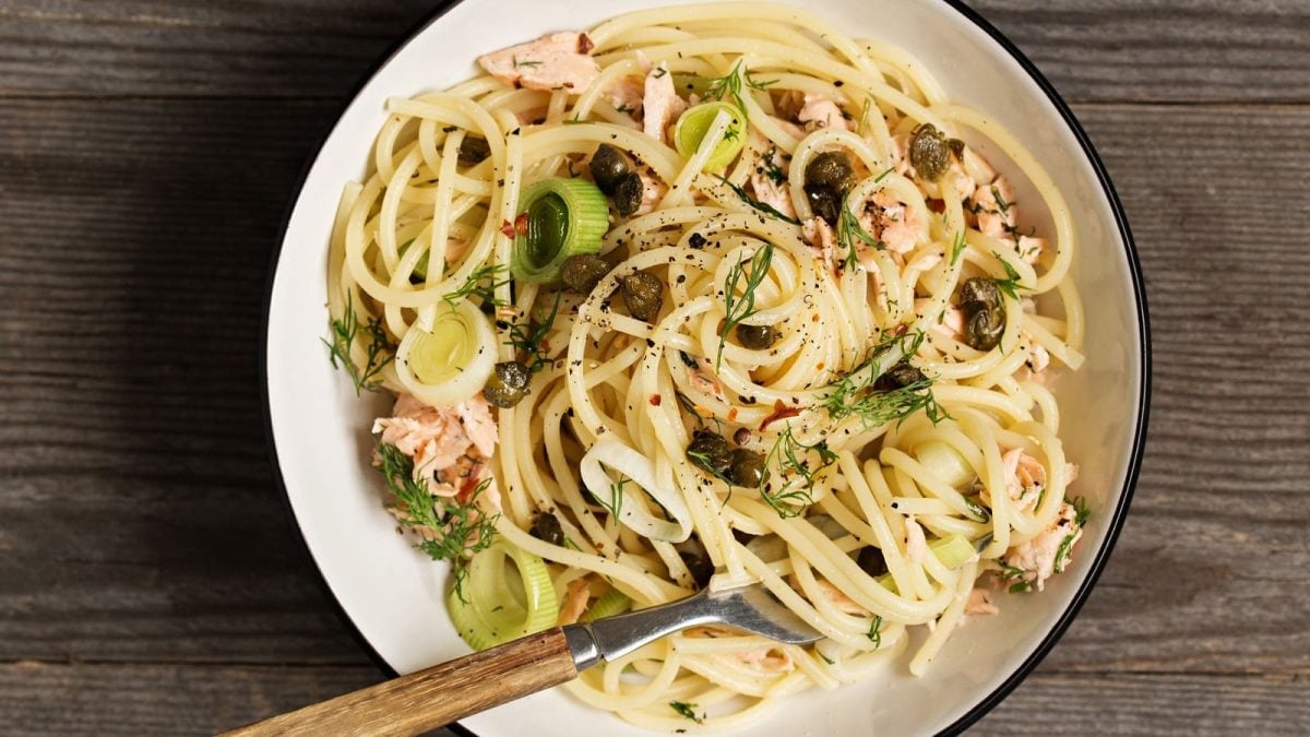 Ein Teller mit Zitronenbutter-Pasta mit Lachs auf einem Holztisch.