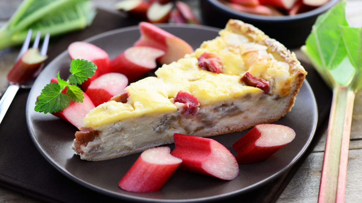 Rhabarber Schmandkuchen mit Rhabarberstücken auf schwarzem Teller.