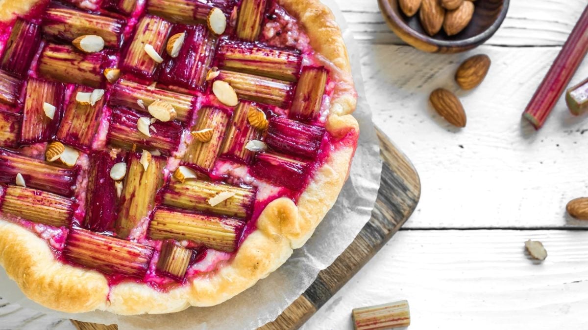 Das Rhabarber Törtchen auf eine kleinen Schneidebrett und weißem Holztisch direkt von oben fotografiert.