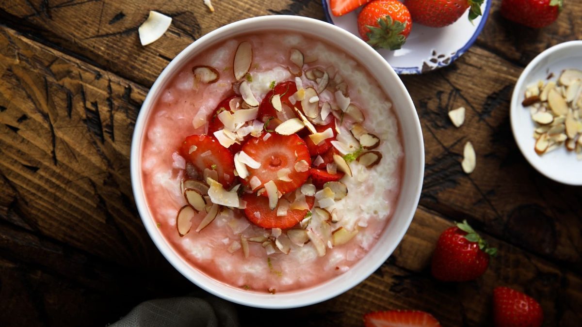 Eine weiße Schüssel mit Rhabarber-Erdbeer-Porridge auf einem dunklen Holztisch.