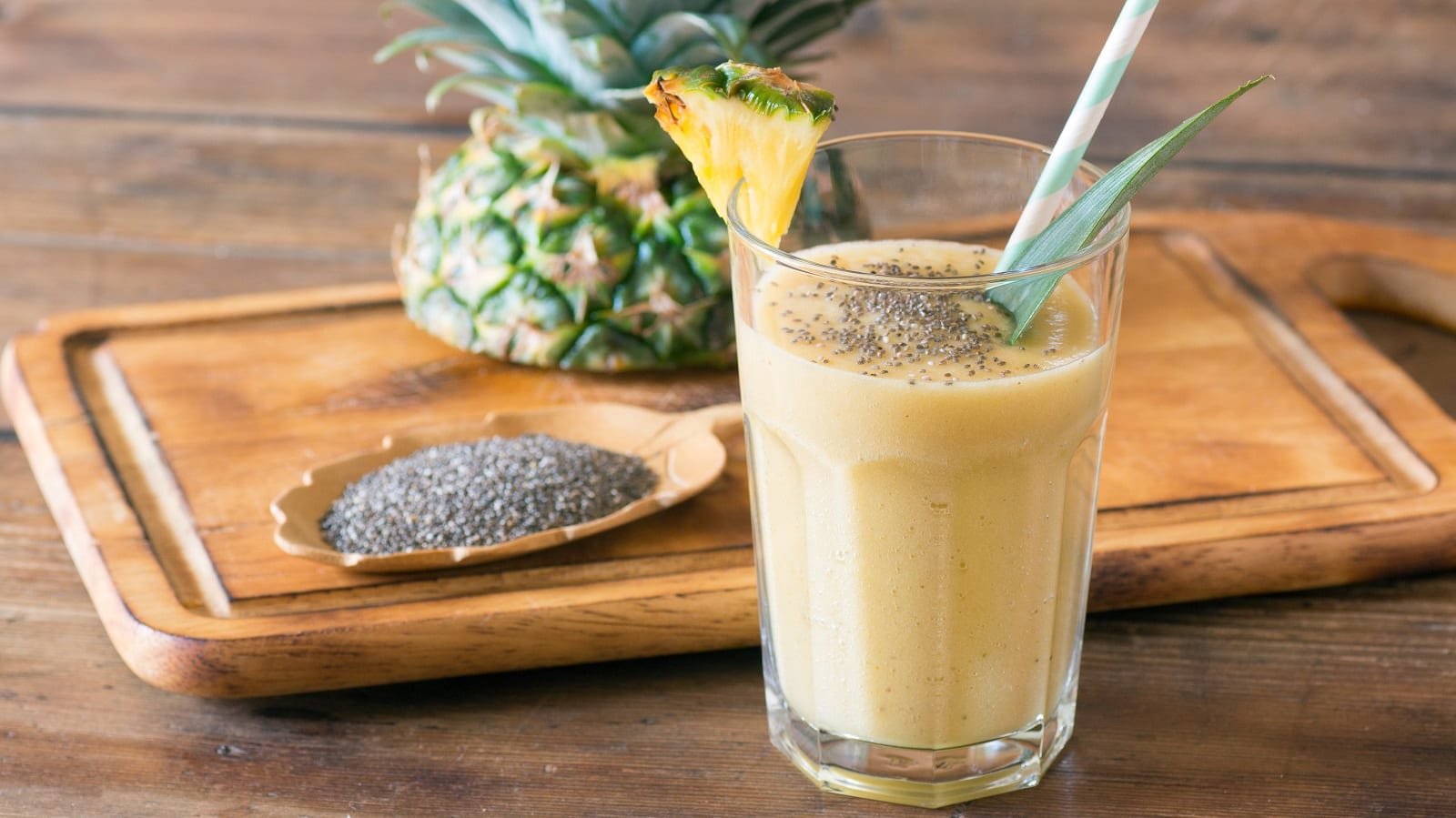 Ein Glas Pina Colada Smoothie vor einem Holzbrett.