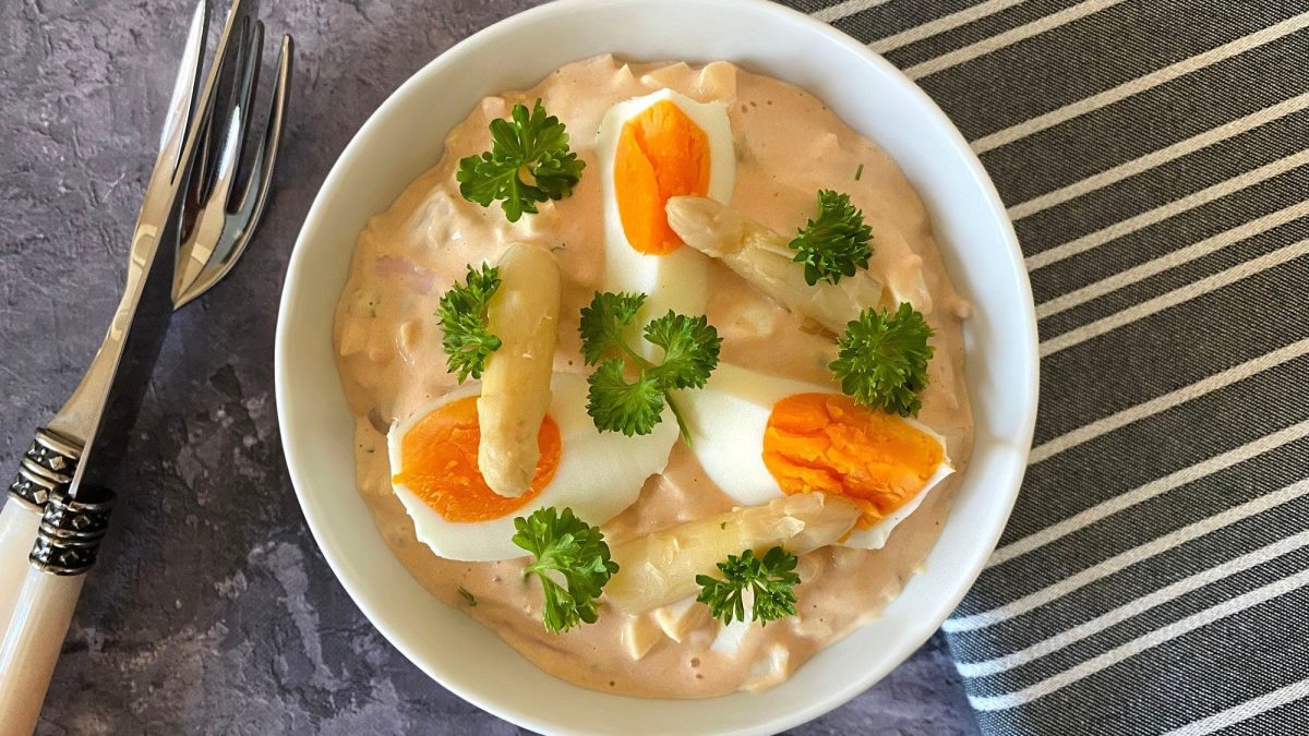 Eiersalat mit Schinken und Spargel in weißer Schüssel.