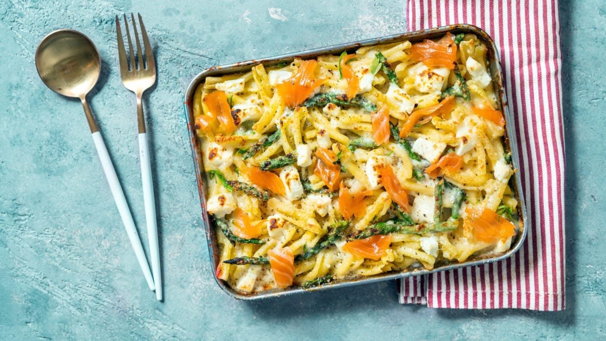 Spargel-Nudelauflauf mit Lachs und Feta auf blauer Tischplatte.