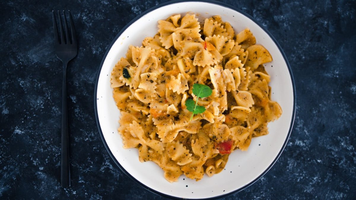 Ein weißer runder Teller mit Tahini-Miso-Pasta auf einem dunkelblauen Tisch.