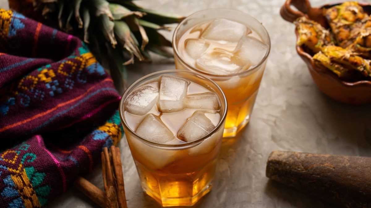 Selbst gemachte Tepache Mexikanische fermentierte Ananas-Limonade in zwei Gläsern mit Zutaten und buntem Stoff im Bild auf hellem Unterrgund. Draufsicht.