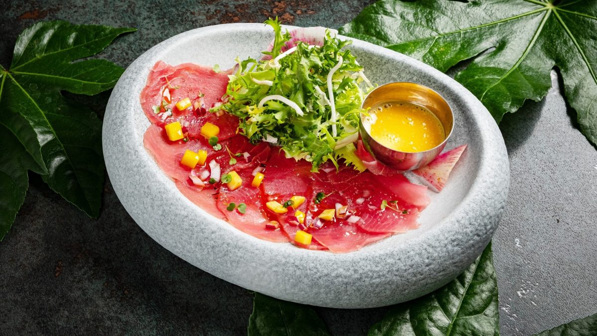 Ein grauer Untergrund mit einem hellgrauen Teller. Darin ist das Thunfisch-Sashimi mit der Mangosauce.