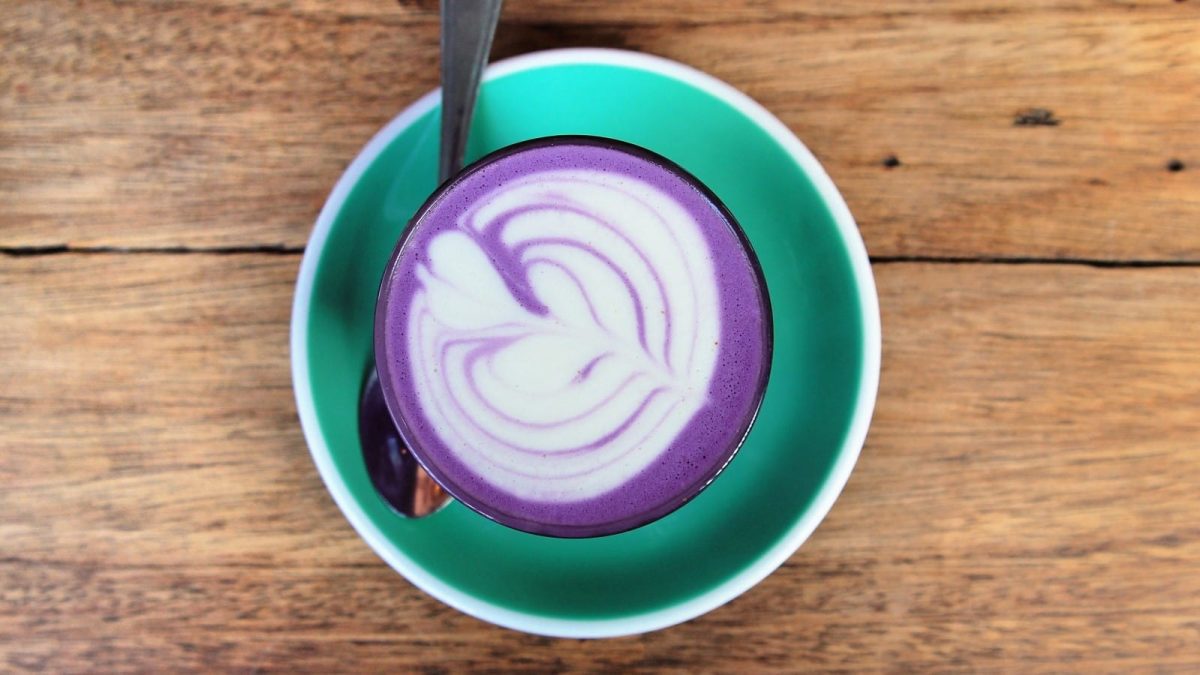 Eine türkise Untertasse mit Ube Latte auf einem hellen Holztisch
