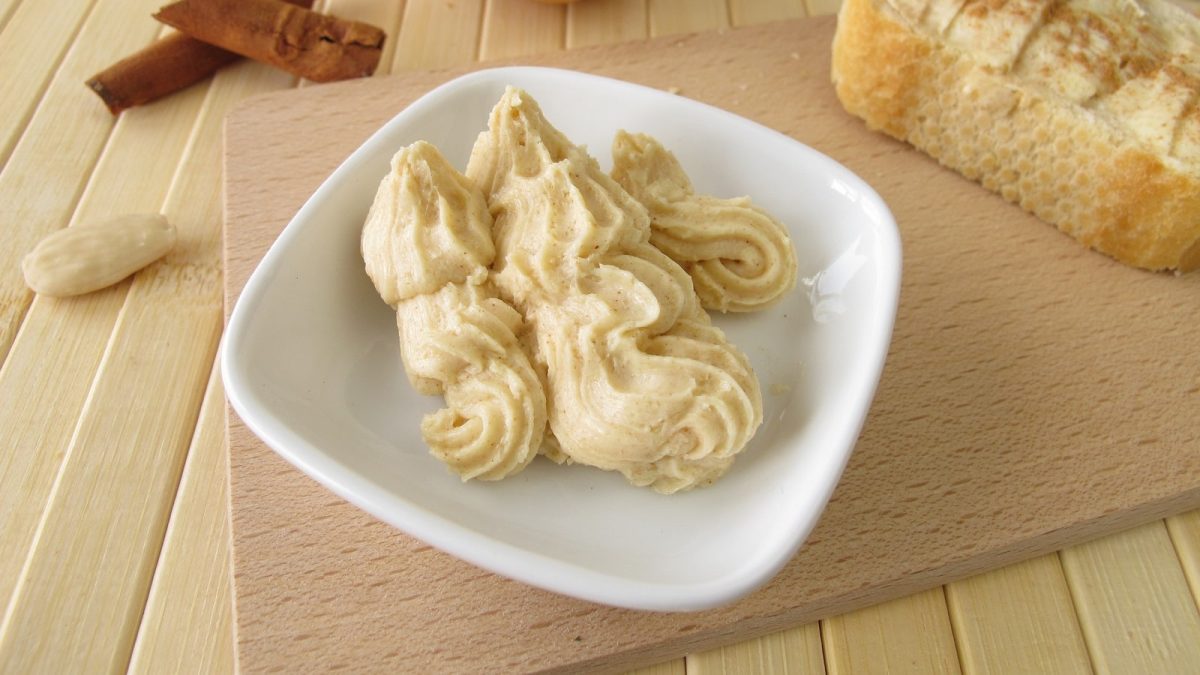 Ein weißer Teller mit Honig-Zimt-Butter auf einem Holzbrett.