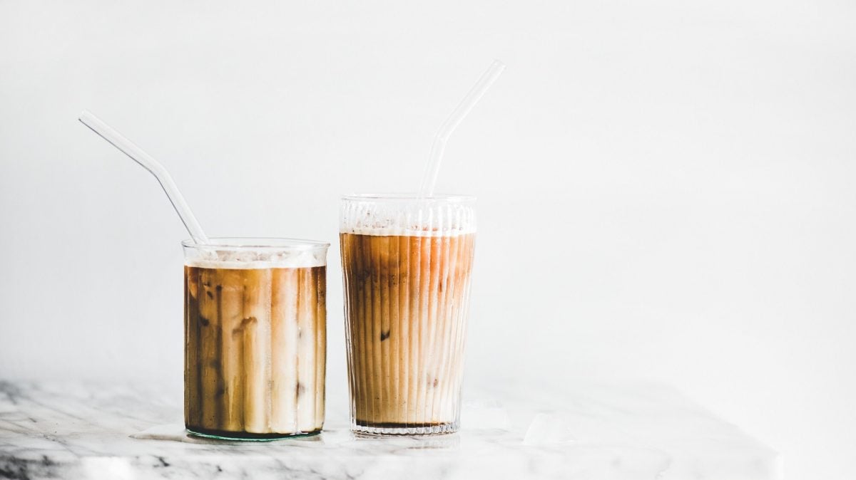 Zwei Gläser Iced Banana Latte mit Strohhalm und Eis auf einem Marmortisch.