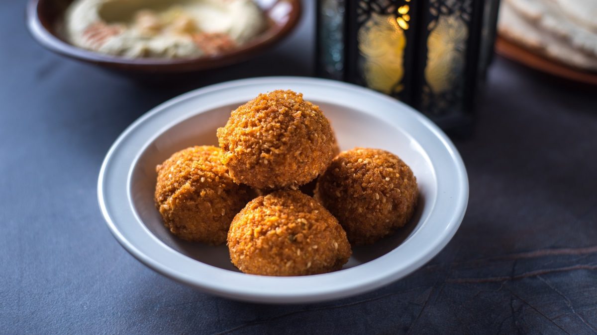 Fünf frittierte Blumenkohlbällchen in einer weißen Schale. Im Hintergrund ein orientalisches Licht und eine Schale mit dem Joghurt-Dip.