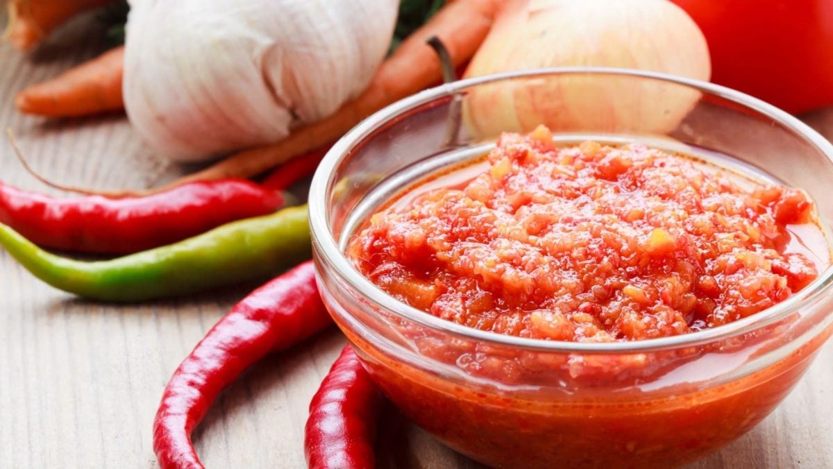 Chines Chili Garlic Sauce in einer Glasschale mit Knoblauch und Chilis auf hellem Untergrund. Draufsicht.