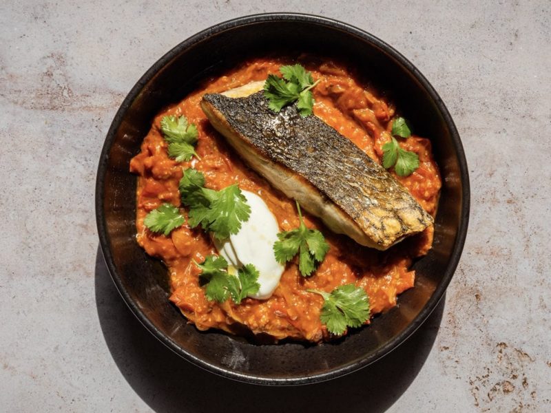 Ein Teller Fischshuka mit einem Fischfilet, Schmand und Petersilie in der Draufsicht.