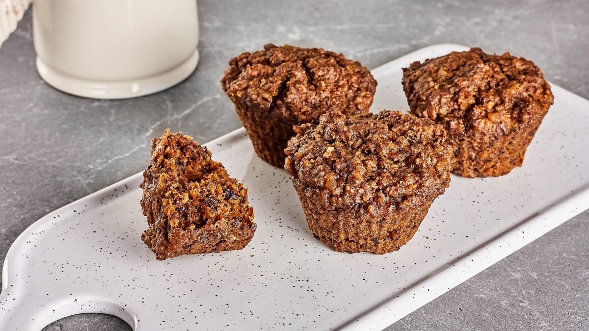 Ein weißes Brett mit den Granola-Muffins auf einem grauen Steintisch. Im Hintergrund weiße Keramik erkennbar.