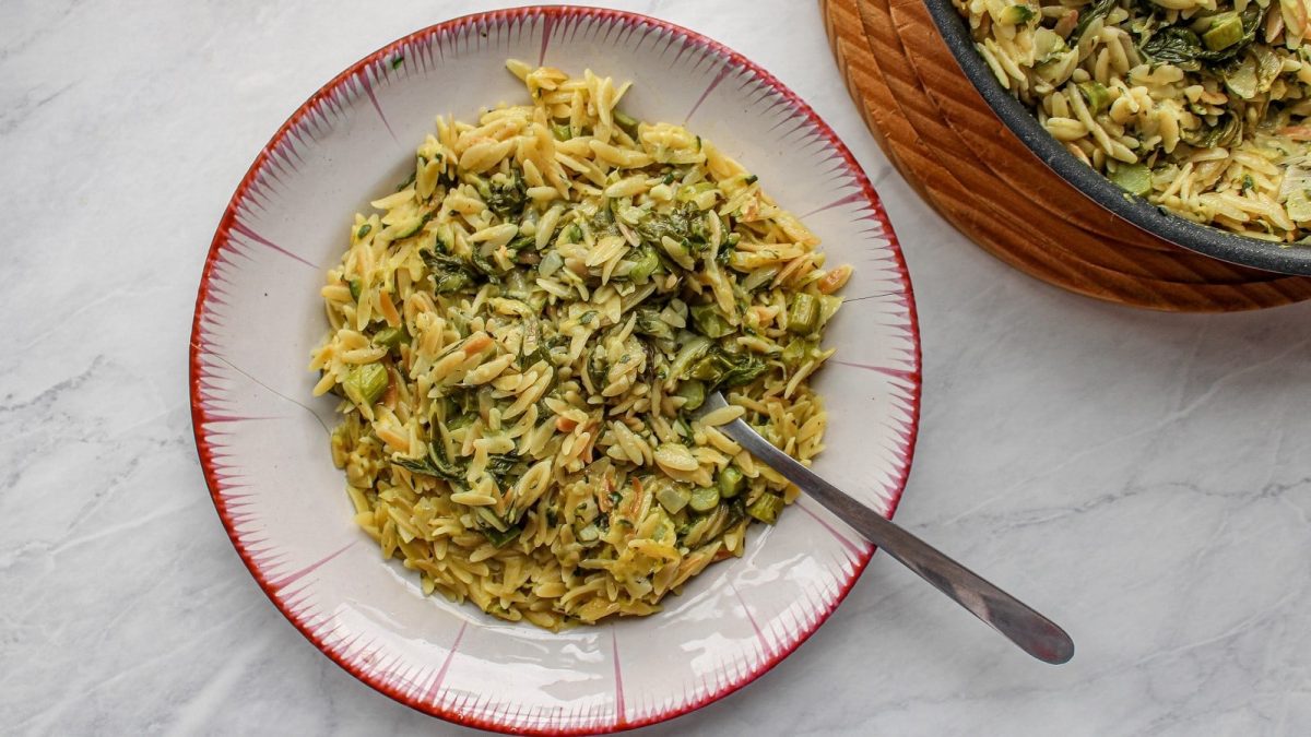 Ein weißer Teller mit Orzo Primavera auf einem hellen Tisch.