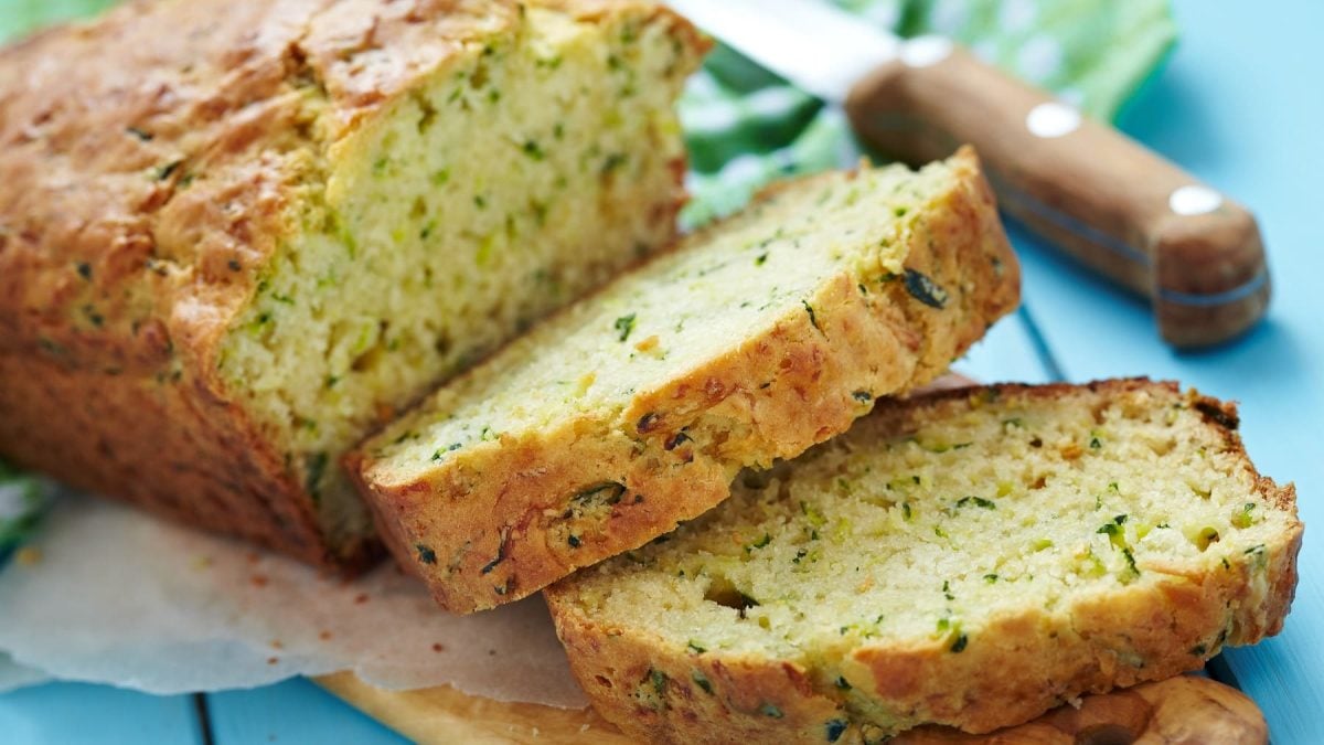 Das Zucchinibrot angeschnitten auf einem blauen Holztisch.