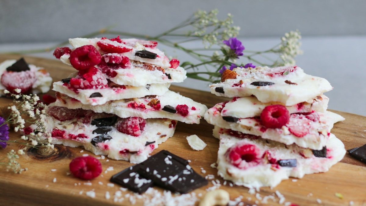 Ein paar Joghurt-Bites mit Beeren auf einem Brett gestapelt, im Hintergrund Blüten.