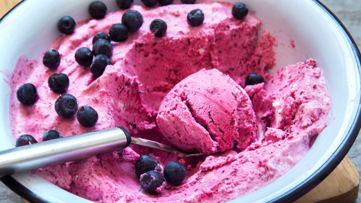 Eine weiß-blaue Schüssel mit dem violetten Blaubeer-Joghurteis und einem Eislöffel.