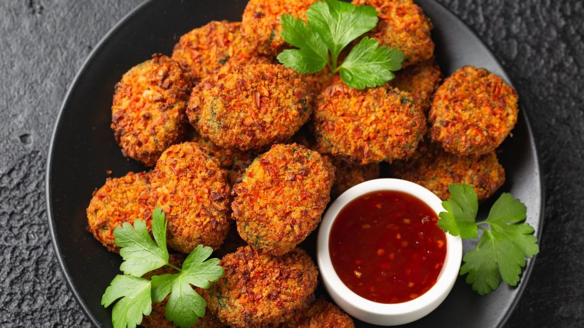 Mehrere Kartoffeltaler auf einem schwarzen Teller und dunklem Tisch mit einem kleinen Schälchen Sweet-Chili-Sauce.