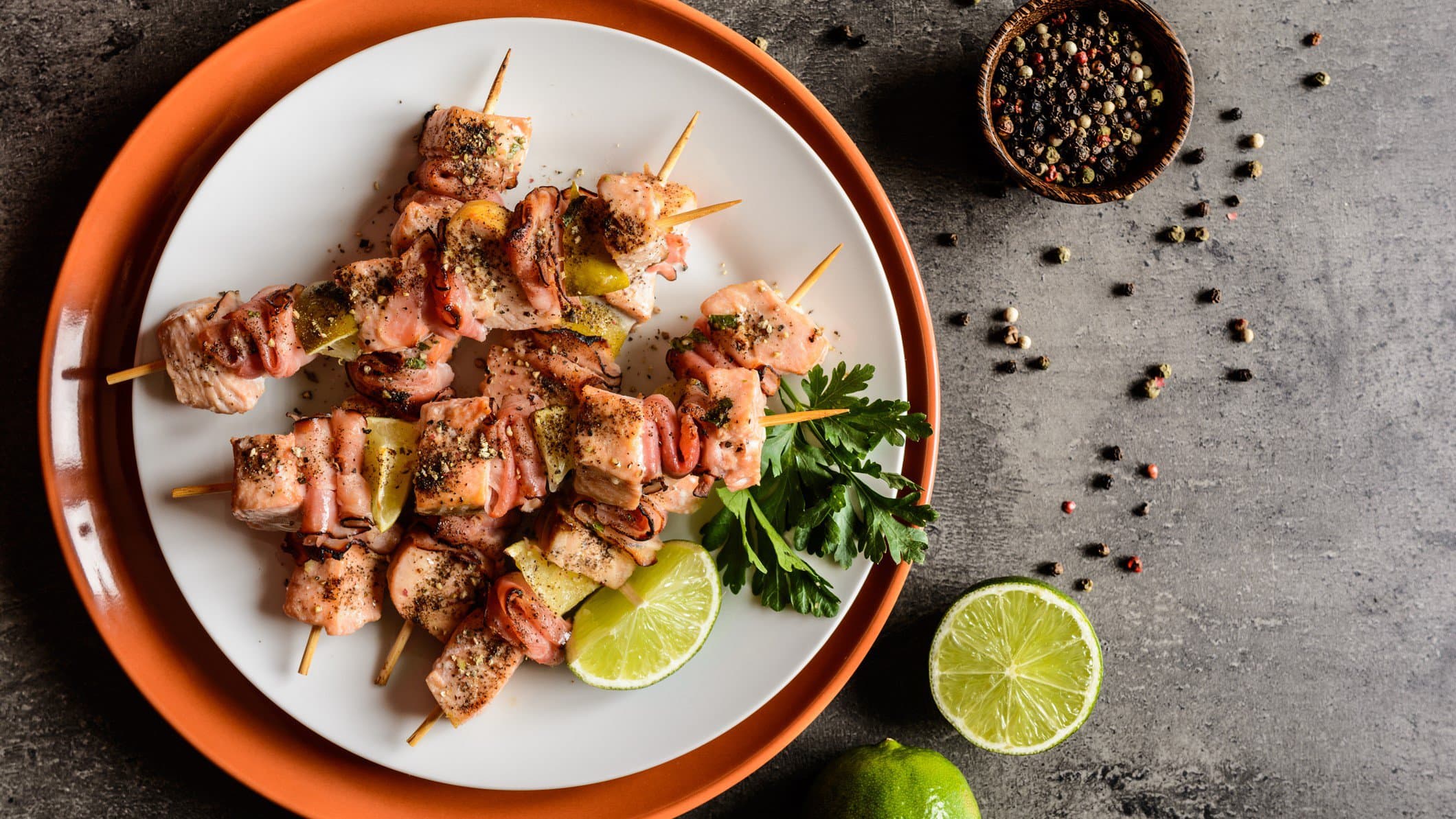 Lachs-Spieße mit Limette auf weißem und braunem Teller.