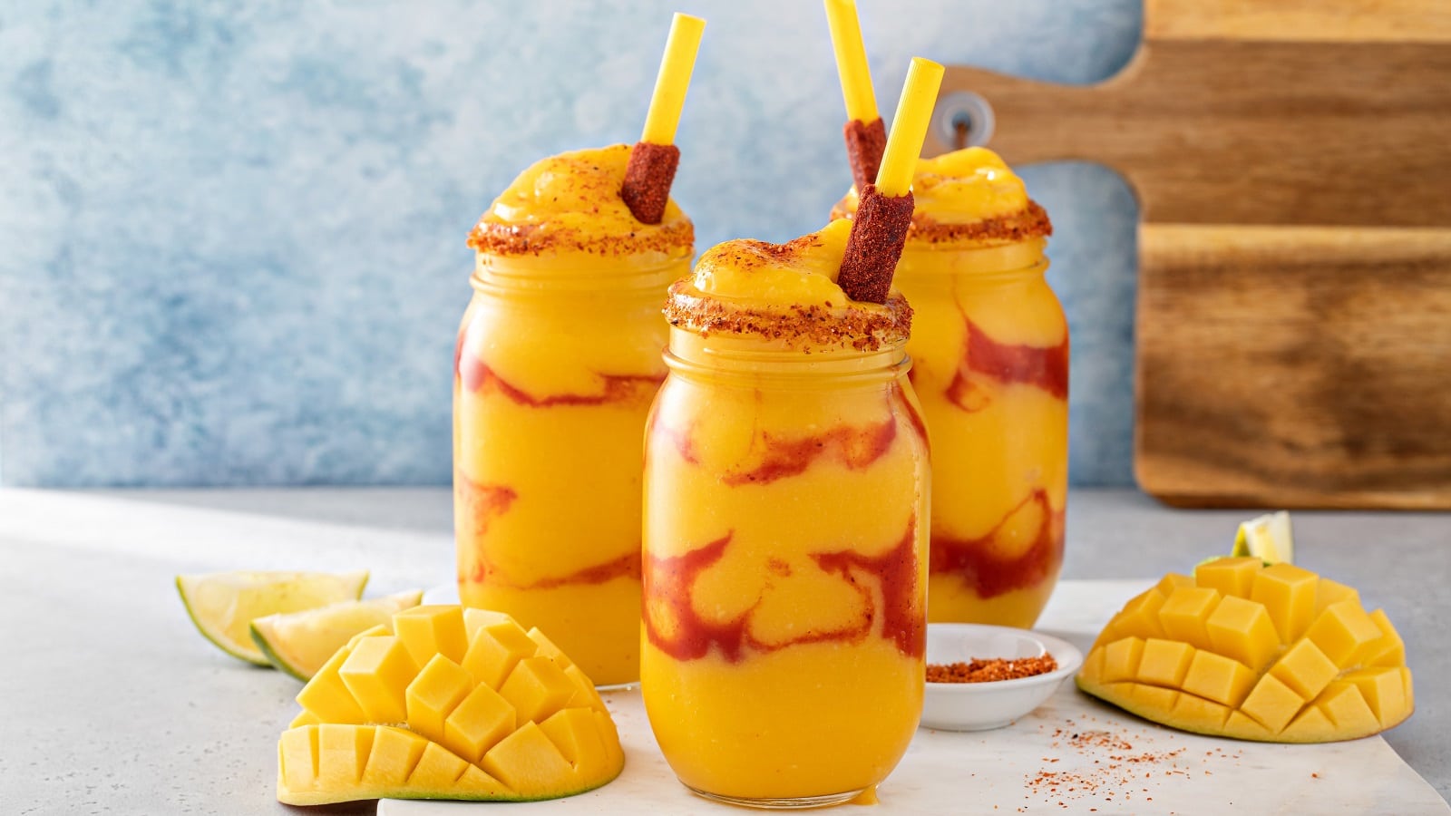 Drei Gläser mit Mangonada vor einem hellblauen Hintergrund.