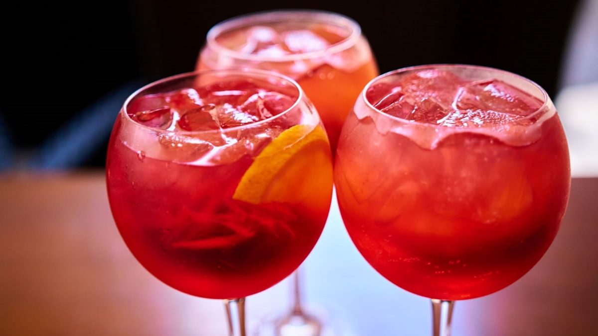 Drei Martini Fiero Lemonade in Ballongläsern auf Holz vor dunklem Hintergrund. Frontalansicht.