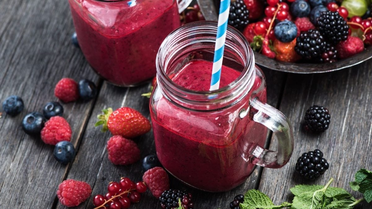 Ein Glas Matcha Berry Smoothie neben frischen Beeren.
