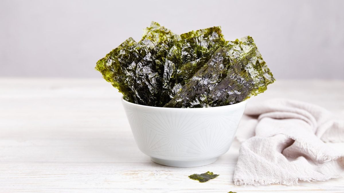 Eine weiße Schüssel mit Nori Chips auf einem weißen Tisch.