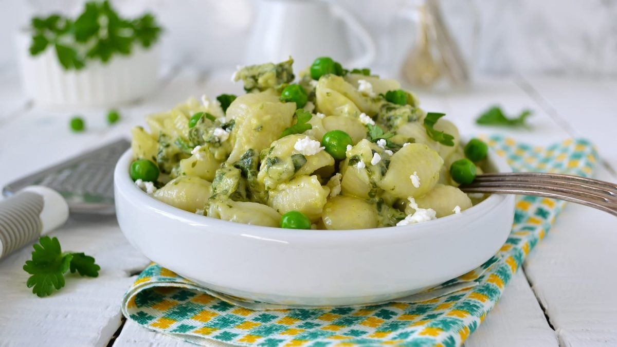 Ein tiefer Teller mit Nudelsalat mit Ricotta und Erbsen.