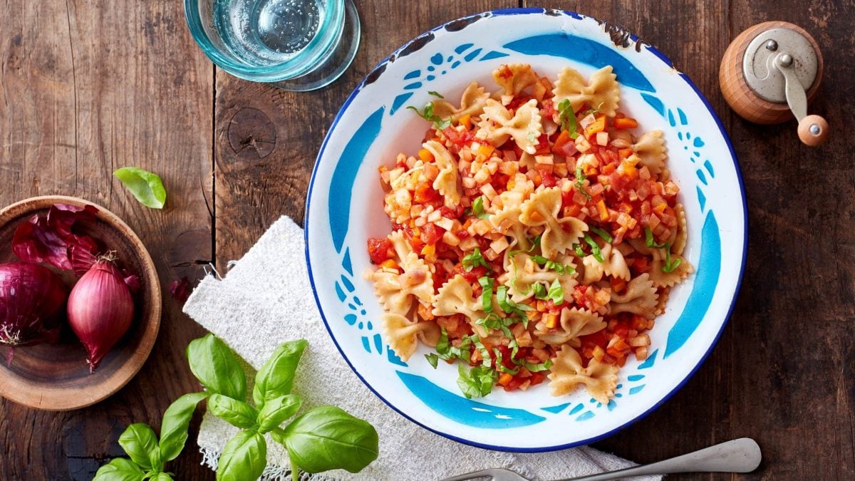 In einer Schüssel ist eine Portion Pasta mit Möhre und Sellerie angerichtet. Sie ist mit Basilikum verfeinert.